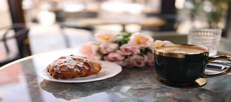 Coffee and a pastry topped with almonds on a marble café table