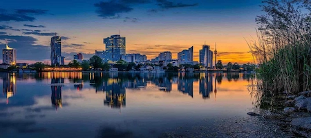 Vienna’s modern skyline reflected in calm water at sunset
