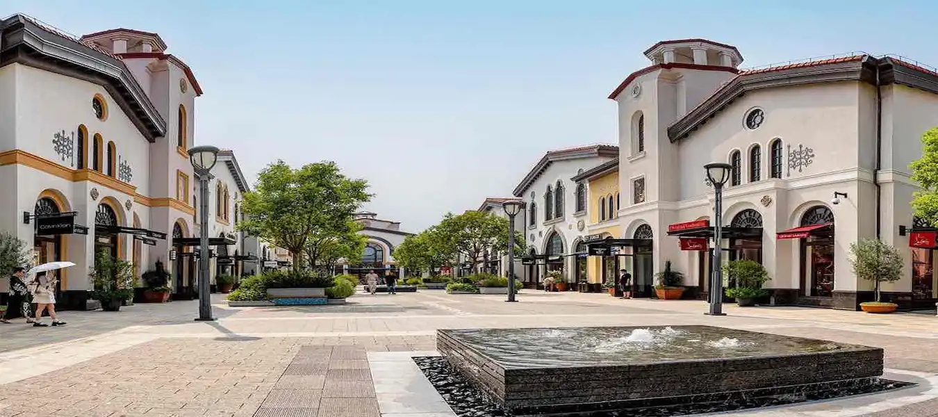 Outdoor designer outlet with arched shopfronts, trees and a fountain