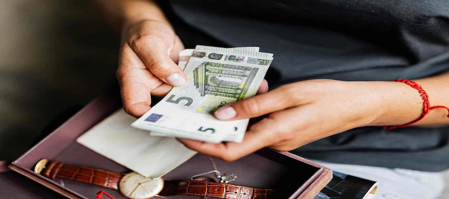 Hands counting euro banknotes over an open box containing a wristwatch