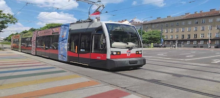 Red and grey Vienna tram beside a stop with colourful paving