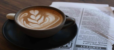 Coffee with latte art beside a newspaper on a wooden table