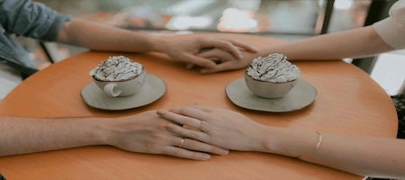 Couple holding hands across a café table beside drinks topped with whipped cream