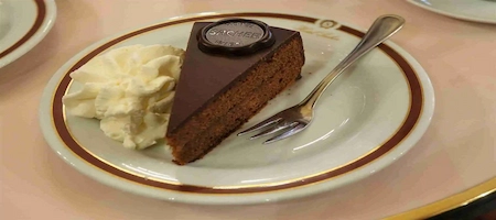Slice of Sachertorte with chocolate glaze and whipped cream on a plate