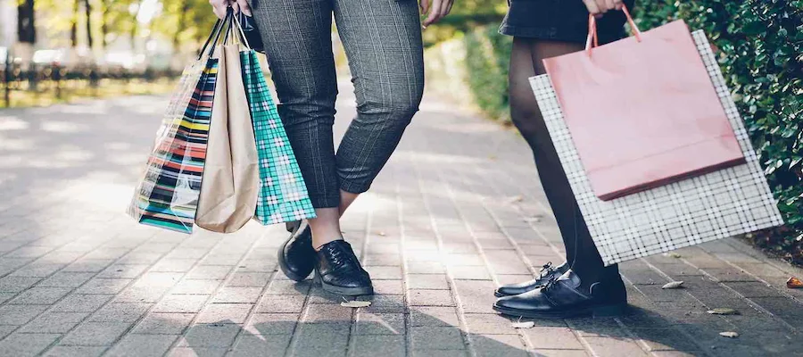Two shoppers holding colourful shopping bags on a paved walkway