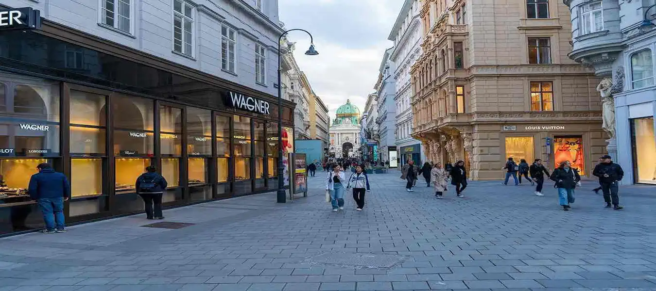 Luxury shops and pedestrians on Kohlmarkt in Vienna, with Hofburg Palace in the distance