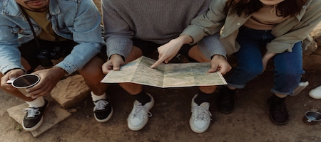 Three travelers looking at a paper map while seated outdoors