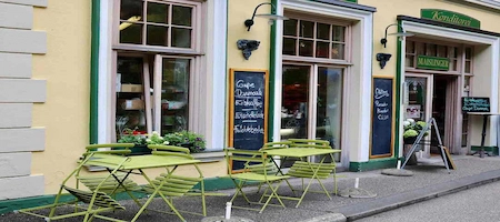Coffeehouse exterior with a yellow façade and green outdoor tables and chairs