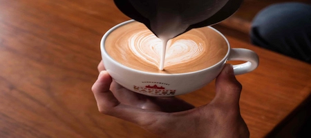 Milk being poured into coffee to create heart-shaped latte art