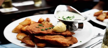 Viennese schnitzel with golden potatoes, a lemon wedge and creamy herb sauce