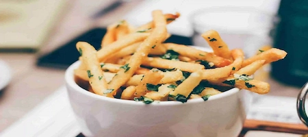 Golden fries sprinkled with chopped herbs in a white bowl