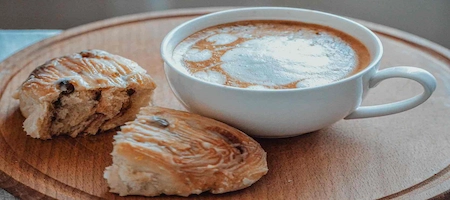 Coffee with milk foam and glazed pastries served on a round wooden tray