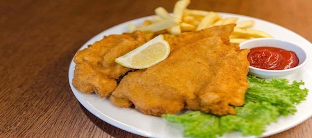Viennese schnitzel served with fries, a lemon wedge, lettuce and ketchup