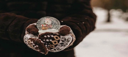Snow globe held in patterned mittens against a snowy background