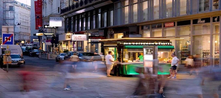 Viennese sausage stand with an illuminated counter and pedestrians passing by