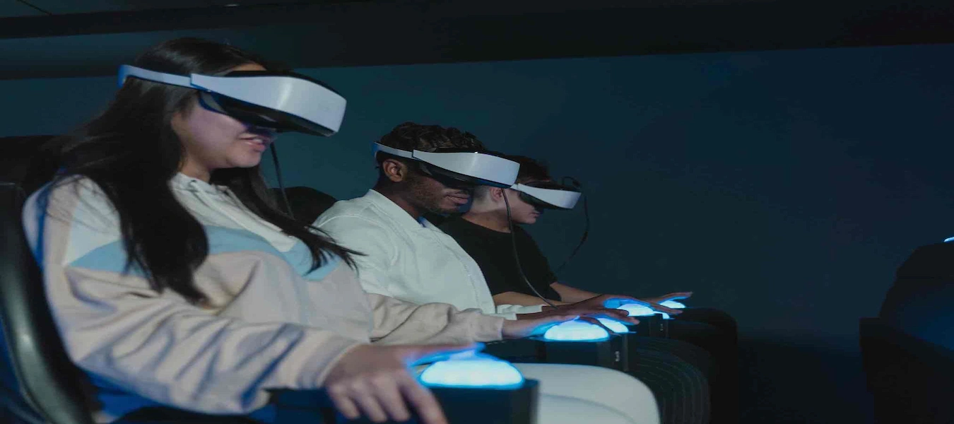 Visitors wearing virtual reality headsets in seats with glowing blue armrests