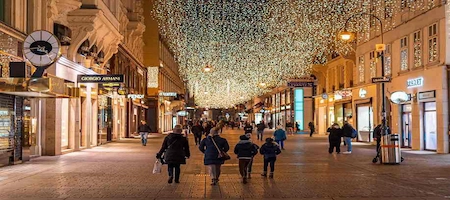 Pedestrians walking along a Vienna shopping street beneath festive lights at night