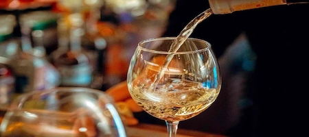 White wine being poured into a stemmed glass at a bar