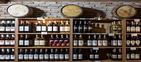 Wine bottles displayed on wooden shelves beneath barrels against a brick wall